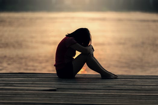 A woman sitting alone on a wooden dock by the lake, showing solitude and reflection.