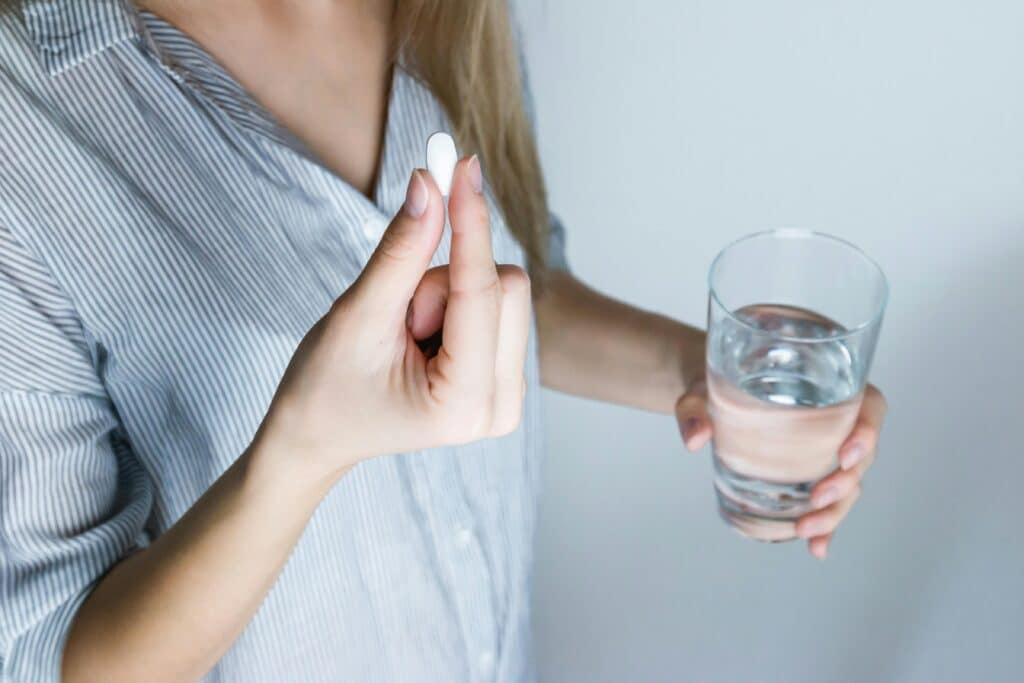 Close-up of a woman holding a pill and a glass of water, ready to take medication.